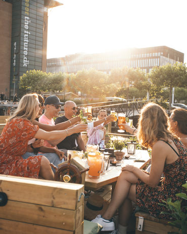 Et selskab af venner skåler glas på en green raft tømmerflåde i solskin
