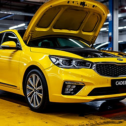 Картинка отражает технический процесс полного обслуживания АКПП Kia Cadenza / K7 (VG): мастер демонтирует поддон, проверяет стружку на магнитах, устанавливает новый фильтр и использует аппарат для полной замены масла. Автомобиль поднят на подъёмнике, в кадре — оборудование, ёмкости для старой жидкости и свежие расходники. Изображение подчёркивает качественный ремонт и точность работы.