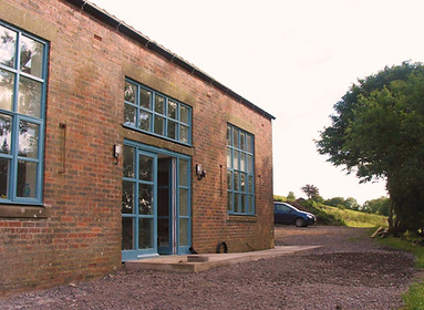 Front of Felldyke Bunkhouse. Brik building with large windows and a gravel parking area.
