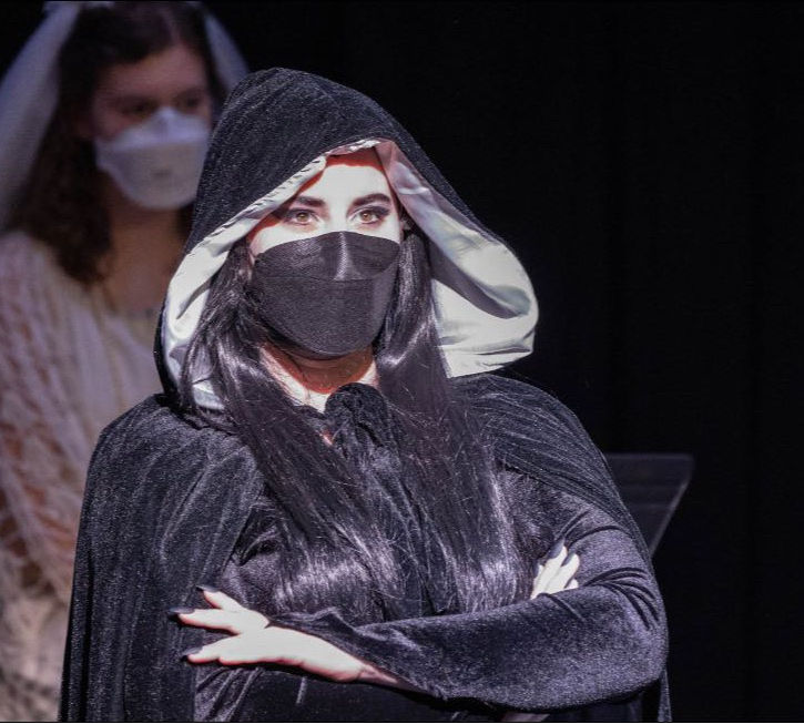 Robyn Emery - Actress
The Addams Family production portraying Morticia Addams in a black cloak, arms crossed, wearing a black mask (covid protocols)