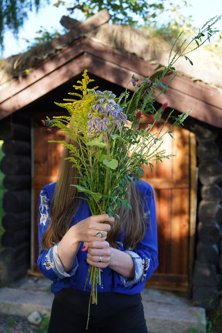 Iris in front of a shed with a bouquet of flowers in front of her face