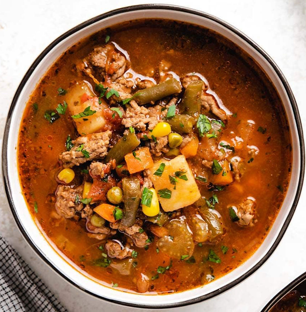 A bowl of vegetable beef soup with chunks of meat, potatoes, carrots, green beans, and corn in a rich broth, garnished with parsley.