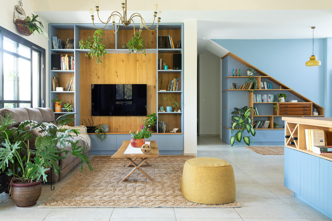 מעיינות של שפע בבית צבועים בתכול: אזור הטלוויזיה השופע עציצים ותקליטים, אזור המדרגות השופע ספרים וידע והאי במטבח