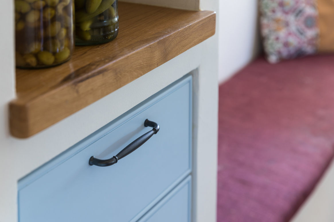 מגירות בגוון תכלת בתוך מטבח בנוי, מעליהן מדף עץ אלון ולצידם ספסל מרופד