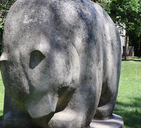 A sculpture of bear with its head bowed and its snout between its two front paws.