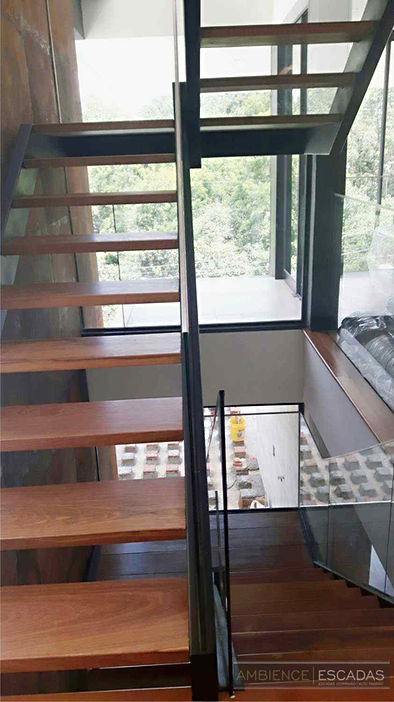 Escadas metálicas dupla em "U" pintada na cor preta com degraus em madeira e guarda corpo em vidro embutido.