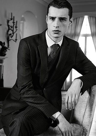 Man posing casually, dressed in a black classy suit with black tie