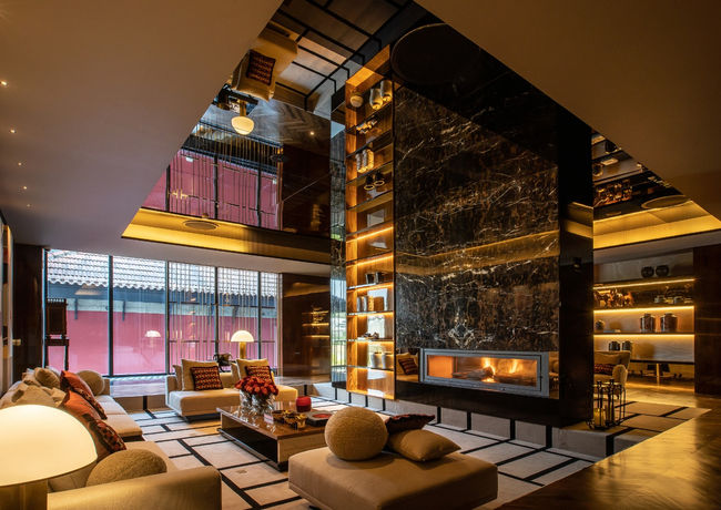 A hotel lobby with very high closets reaching until the first floor and dividing the lobby in two parts. The lobby also has a fireplace and several lounge corners with soft illumination.