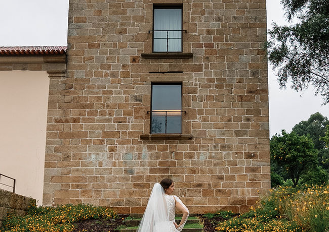 Bride with a long lace train and veil stands on the stairs, facing a classic tower