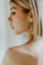 Woman looking over her shoulder showing a thin long golden earring with blue gems