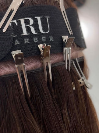 Close up of hair clips and styling tools attached to a stylist’s apron, with salon branding visible in the background.
