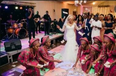 Guests spraying money on a couple dancing at a Nigerian wedding while attendants collect cash from the floor.