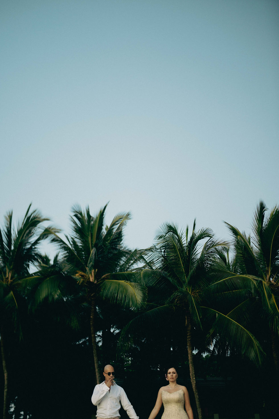 Bride and groom walking beneath palm trees in Zanzibar, cinematic destination wedding photography by Michal Dzikowski