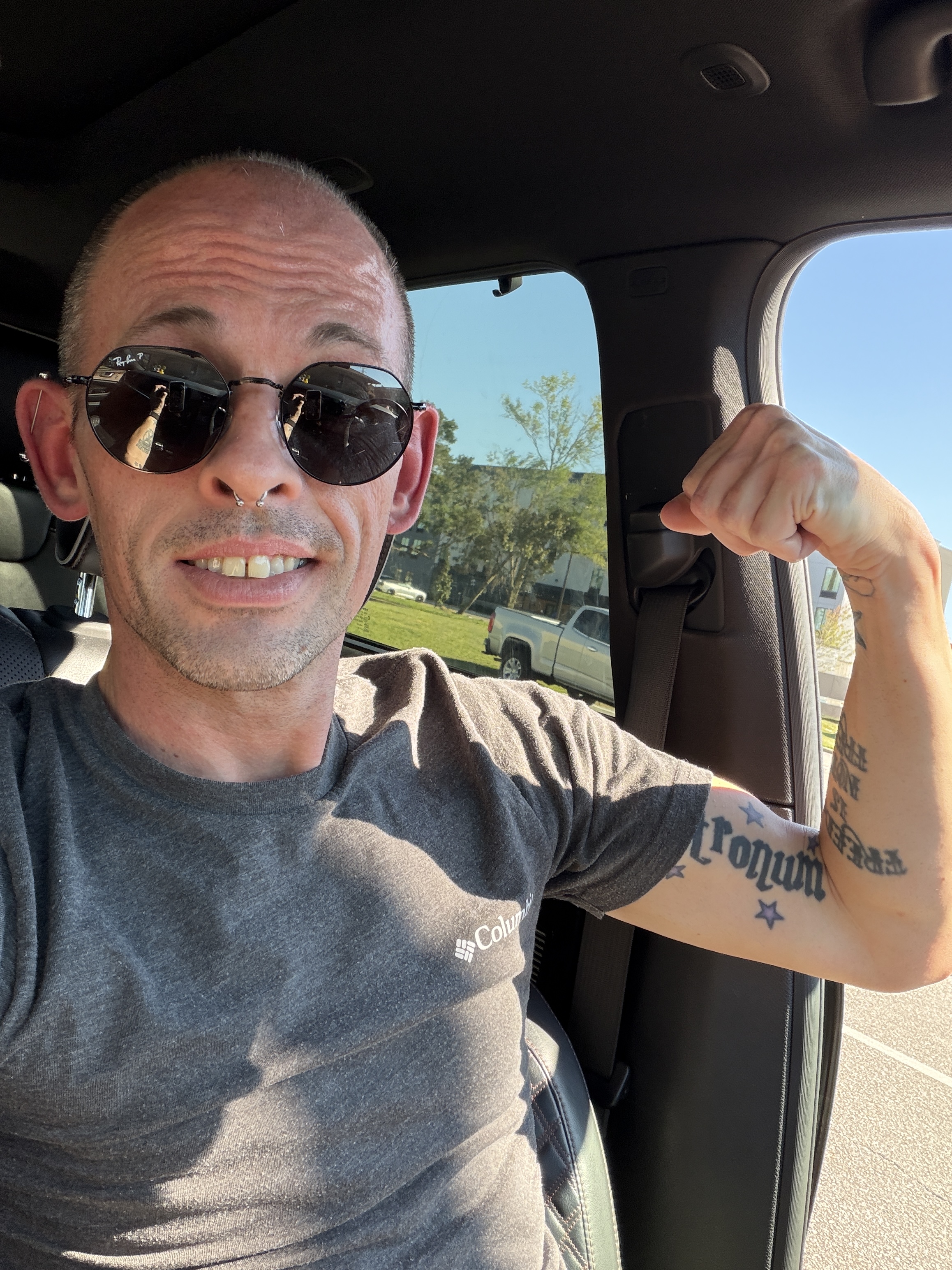 Matthew smiling in sunglasses and flexing his arm in a car.