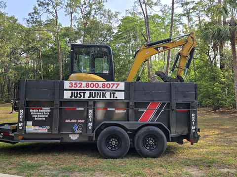 Yellow excavator loaded on trailer with text 352.800.8077 JUST JUNK IT.