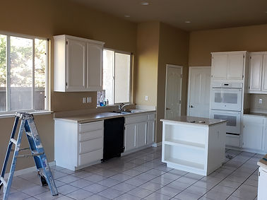 kitchen painted a tan color with white cabinets and painters ladder set on the floor