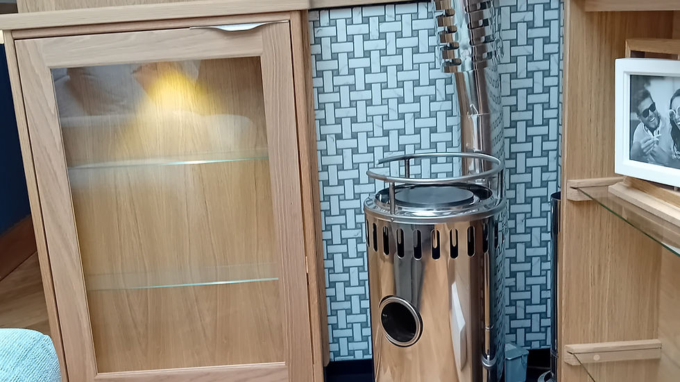 Cozy indoor setting with a shiny metal stove against a woven-patterned wall. Wood flooring, wooden cabinets, and a framed photo visible.
