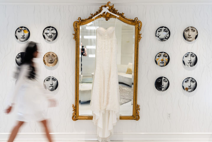 Wedding dress hanging on a gold ornate mirror with modern face art on the wall, as the bride walks by in motion blur at Crystal Plaza in New Jersey, photographed by George Pompilio