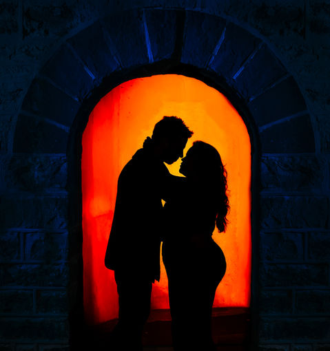A silhouette of a couple in an intimate embrace, framed by an arched stone doorway with a glowing orange background.