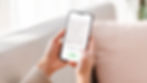 Hands holding a smartphone displaying a Q&A app on infant food allergies. The background features a soft, beige couch.