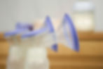 Close-up of two breast pump bottles standing, clear and purple, and with an unfocused background.