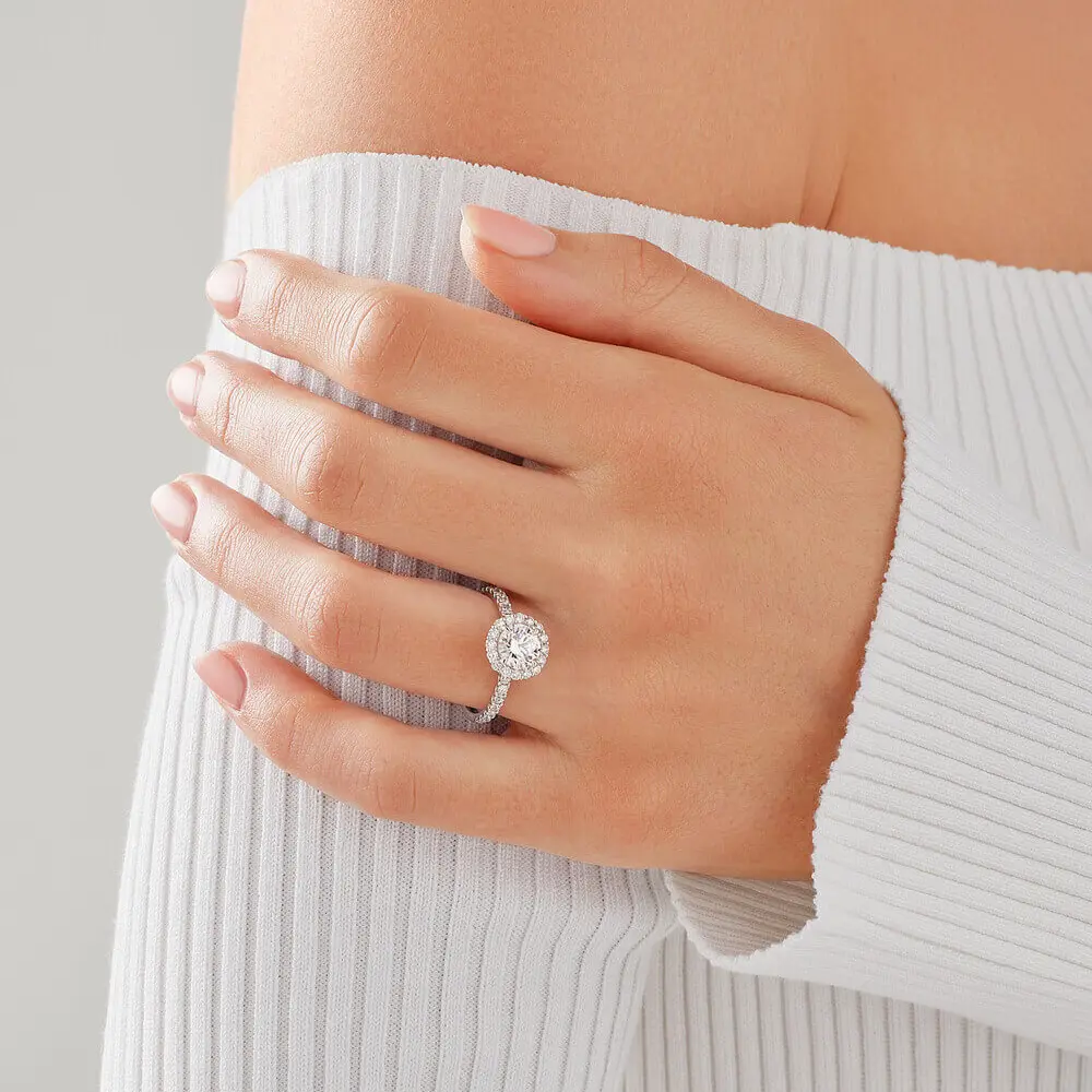 Anillo de compromiso con pave y halo de diamantes en mano de mujer