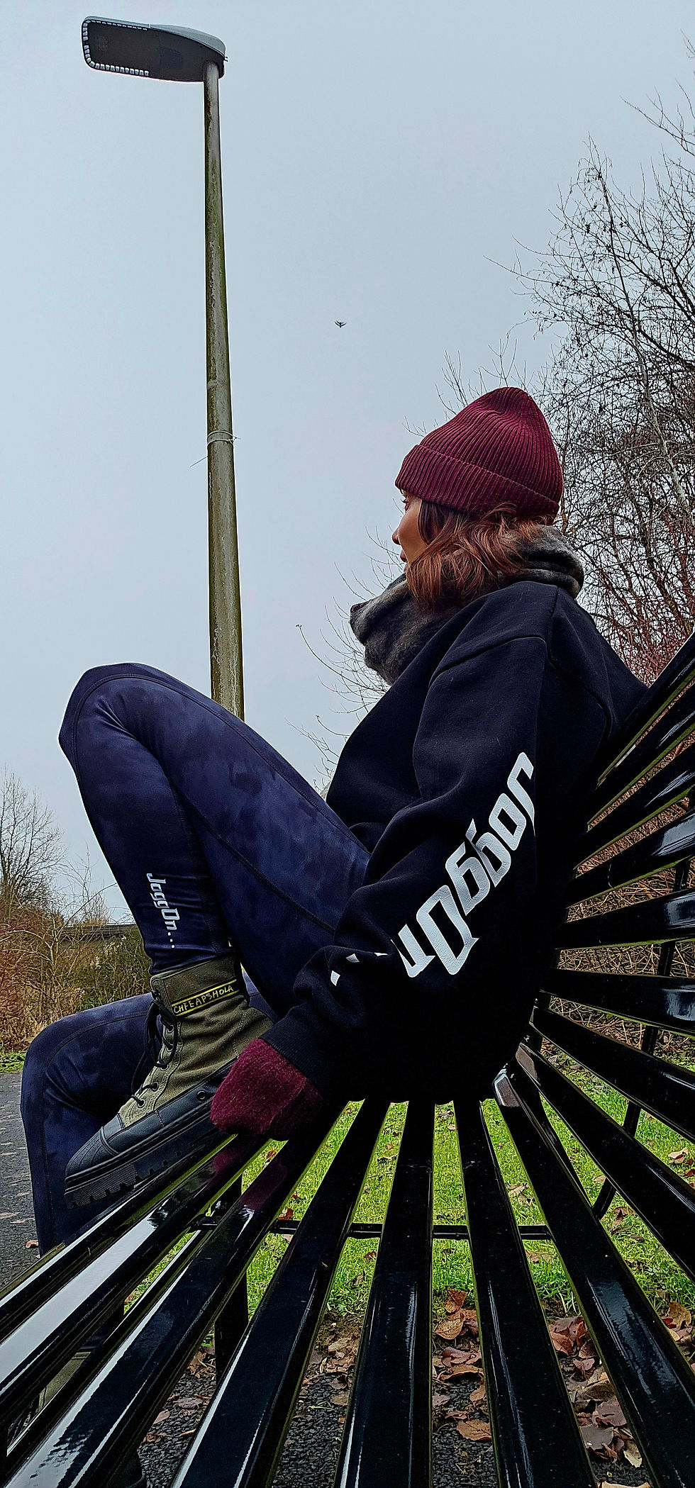 Woman in a heavy sweater and beanie on a park bench.