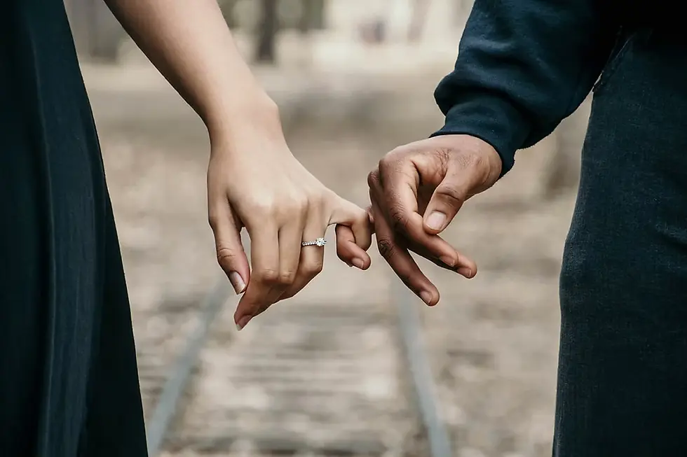 Close-up of two people linking pinkies, one wearing an engagement ring, on a blurred outdoor path with a romantic mood.