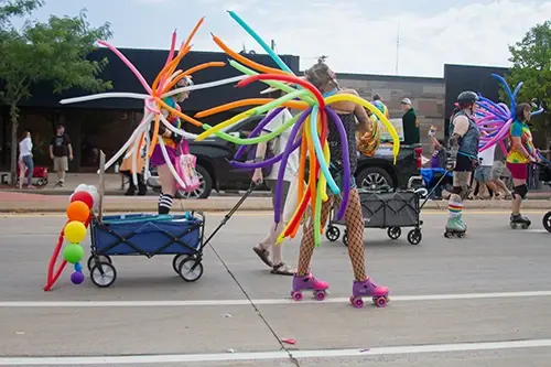 Pride parade participants roller blading down tower avenue with balloon back packs.