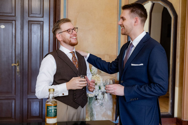 Uśmiechnięty Mateusz w kamizelce rozmawia z gościem przy whisky.