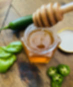 Honey in a glass container with a honeycomb wood stick out of it with basil and Serrano around it on a wood table