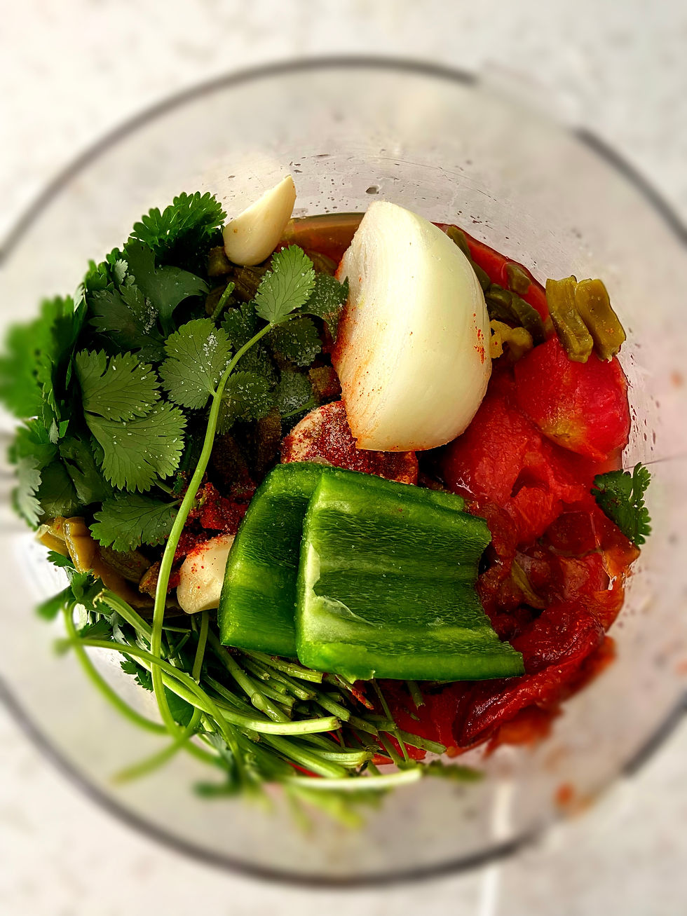 All of the ingredients for smoked cactus salsa ready to be blended in a food processor on a white table