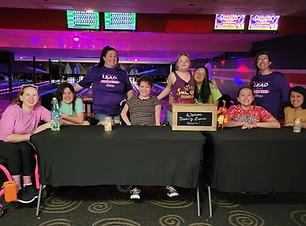 Image of disabled women and girls sitting behind a table with a bowling alley behind them.