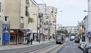 Tram passant dans une rue animée avec des bâtiments modernes et des commerces à Joué-lès-Tours.