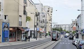 Tram passant dans une rue animée avec des bâtiments modernes et des commerces à Joué-lès-Tours.