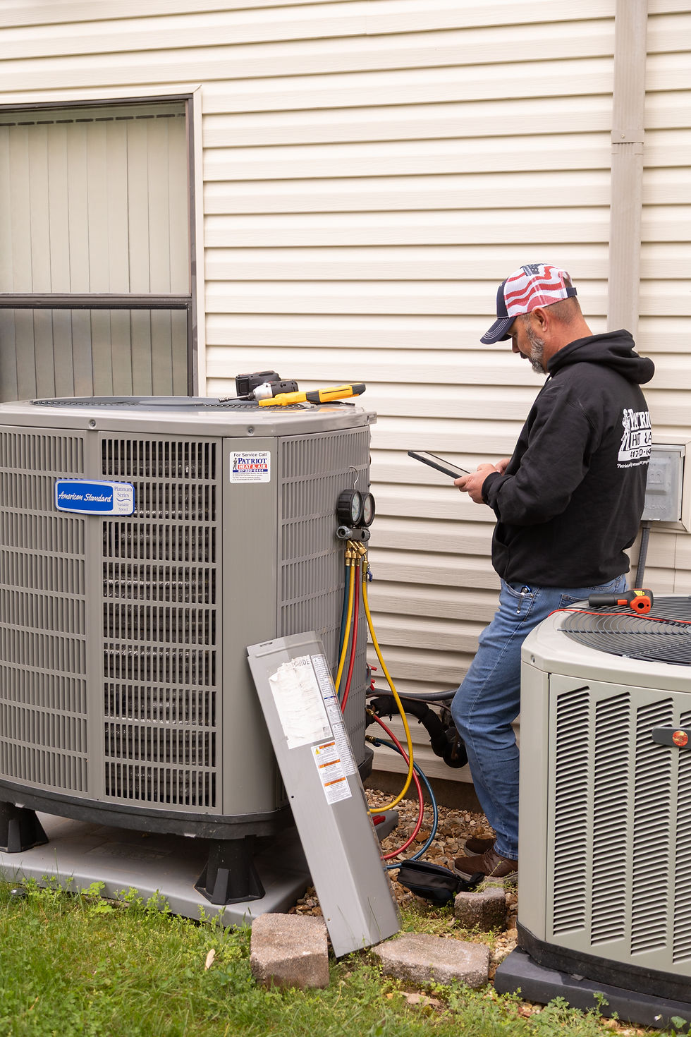 Patriot Heat & Air technician performing diagnostics on an outdoor HVAC unit.