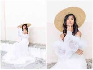 Woman in a white dress and large straw hat sits on a stone bench. The background is a pale wall. The mood is serene and elegant.