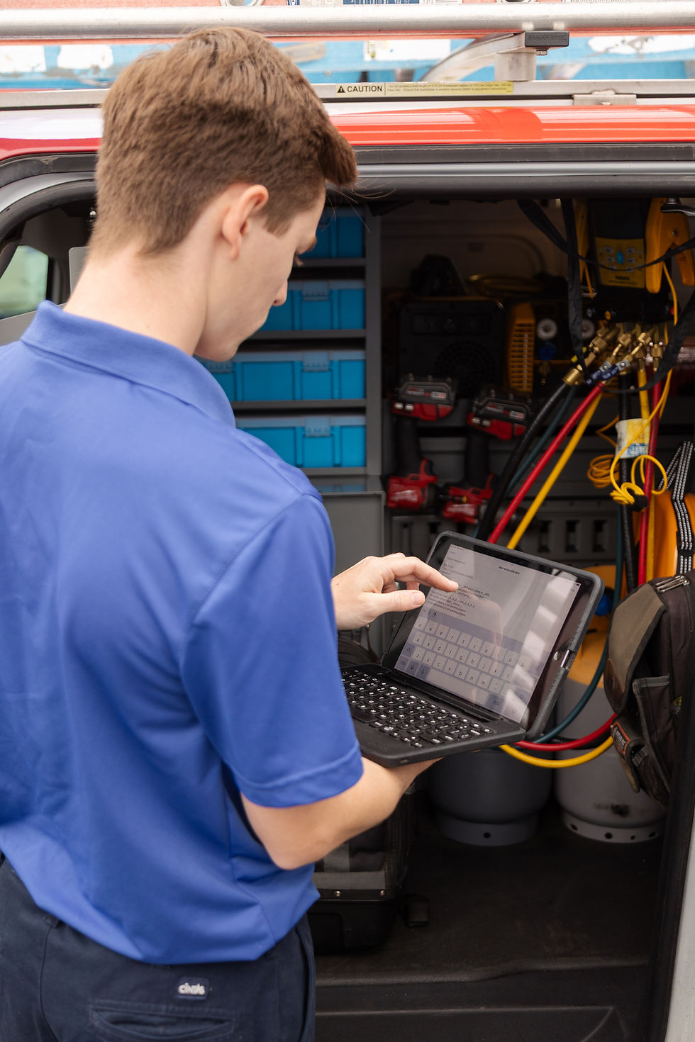 HVAC technician using a tablet to run diagnostics on service equipment from a work vehicle.