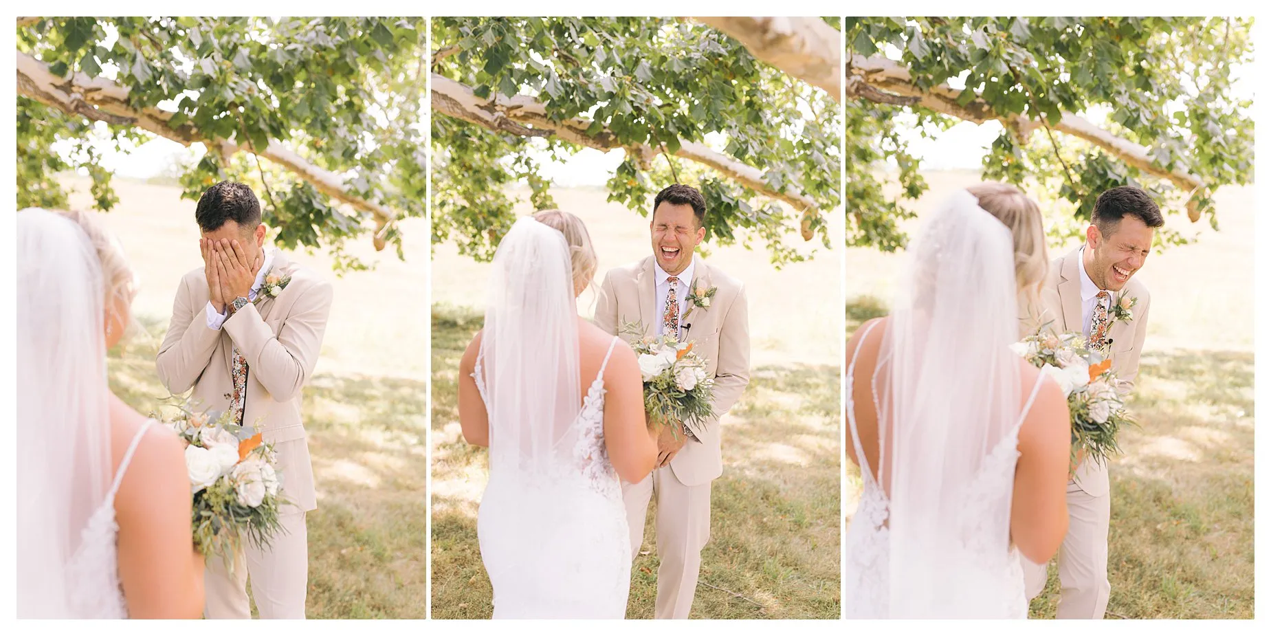 Bride in white dress approaches groom in beige suit under a leafy tree. He covers his face then laughs joyfully, holding a bouquet.