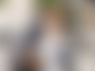 A smiling couple embraces playfully in a stylish courtyard. She's in a white dress, he's in a suit. Chic decor with striped umbrellas.