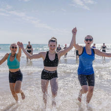 Drei Frauen laufen lachend durch das Meer bei einem gemeinsamen Workout im Aktivurlaub