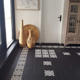 Hal met zwarte vloertegels geverfd als border met witte verf geverfd met tegelontwerp Bailey sjabloon. Ook witte muur met witte deur, decoratie voor raam en kast tegen muur te zien.
