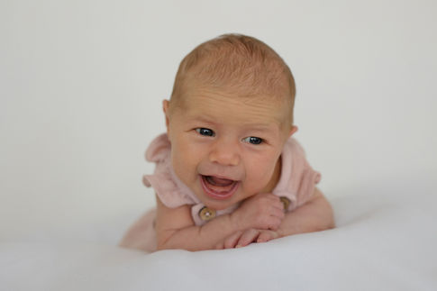 Fröhliches Baby in rosa Kleidung lachend auf weisser Decke liegend.