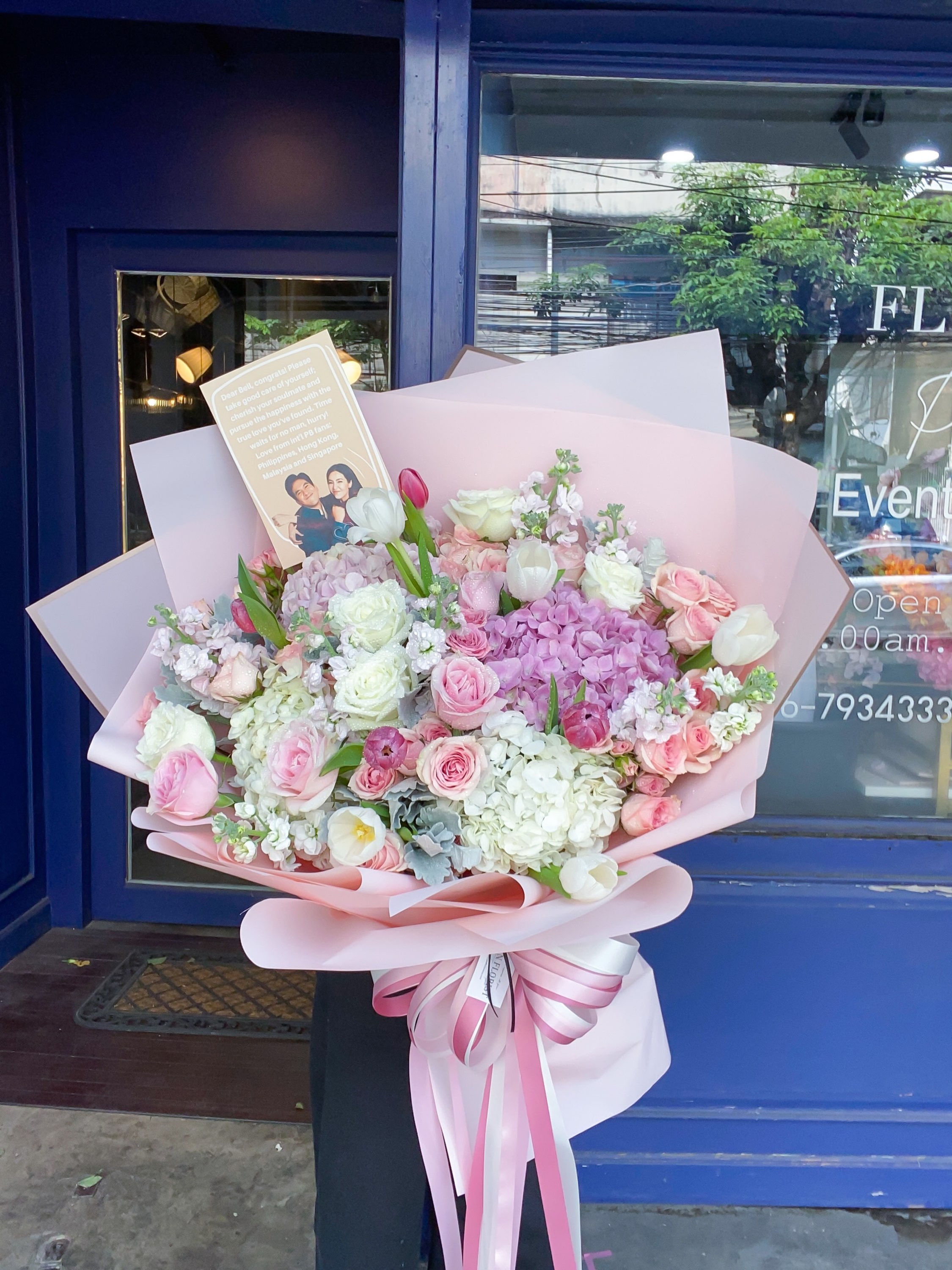 Elegant pink and white bouquet featuring hydrangeas, roses, tulips, and filler flowers, wrapped in blush paper with a ribbon.