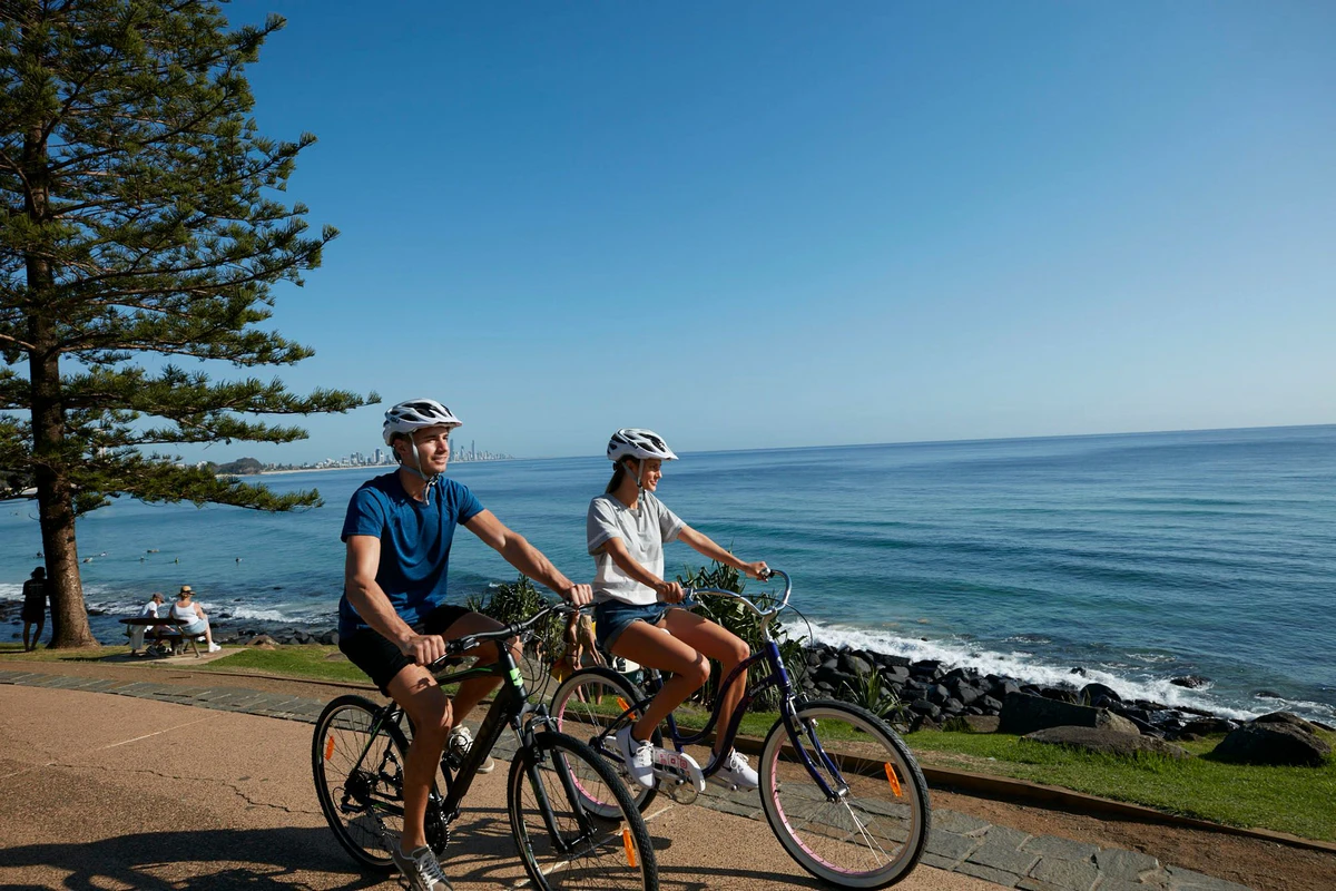 couple-cycling-burleigh-headland-ocean-rocks-skyline-nearby-burleigh-gold-coast-motel.webp