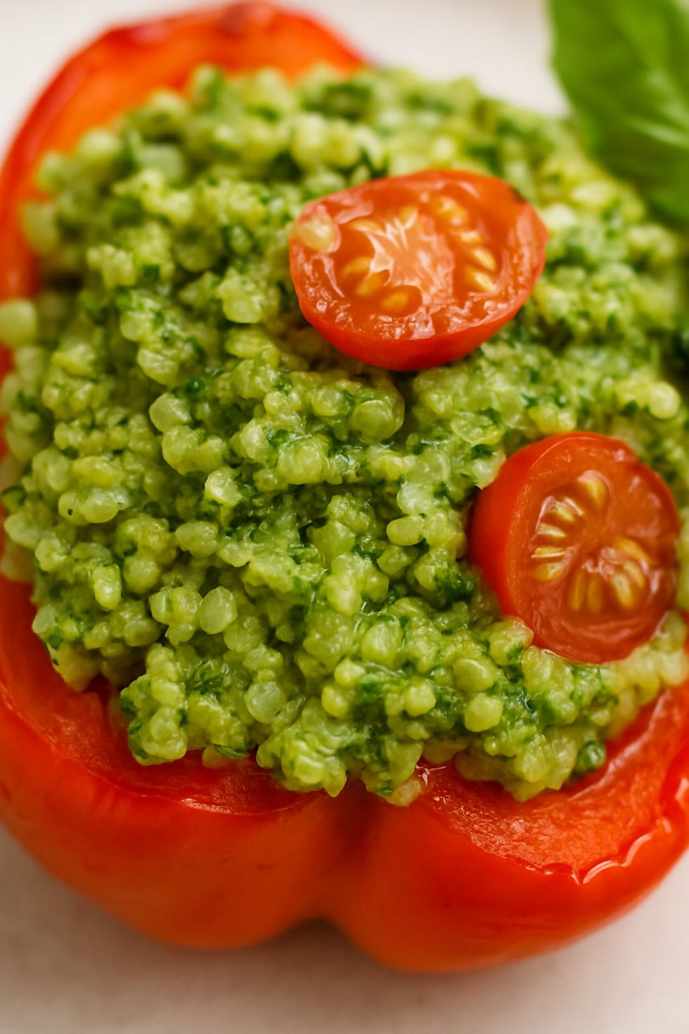 Halved roasted peppers filled with bright green garlic-free pesto quinoa, garnished with fresh basil.