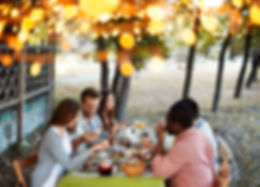 Five people having an outdoor dinner under warm lights
