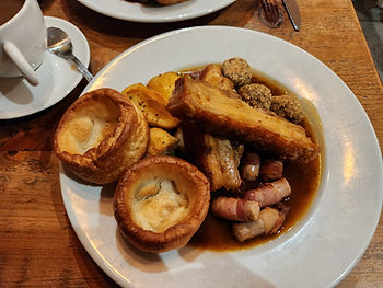 Plate of Yorkshire puddings, roast potatoes, stuffing balls, and meat in gravy on a wooden table. A cup of tea is in the background.