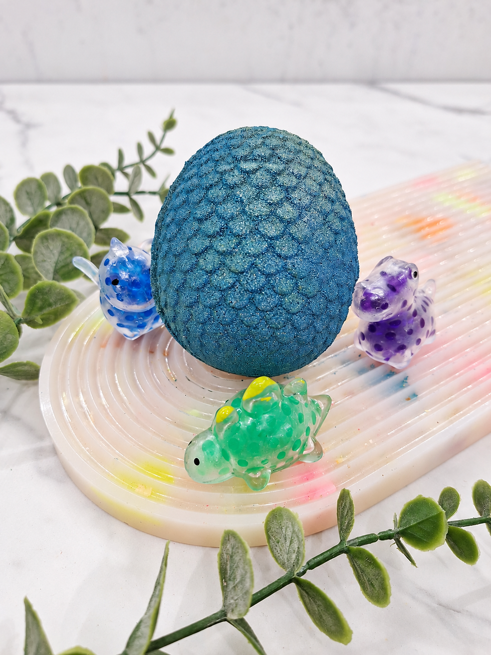 Scaled dinosaur egg bath bomb with three example dinosaur squishies, one toy included
