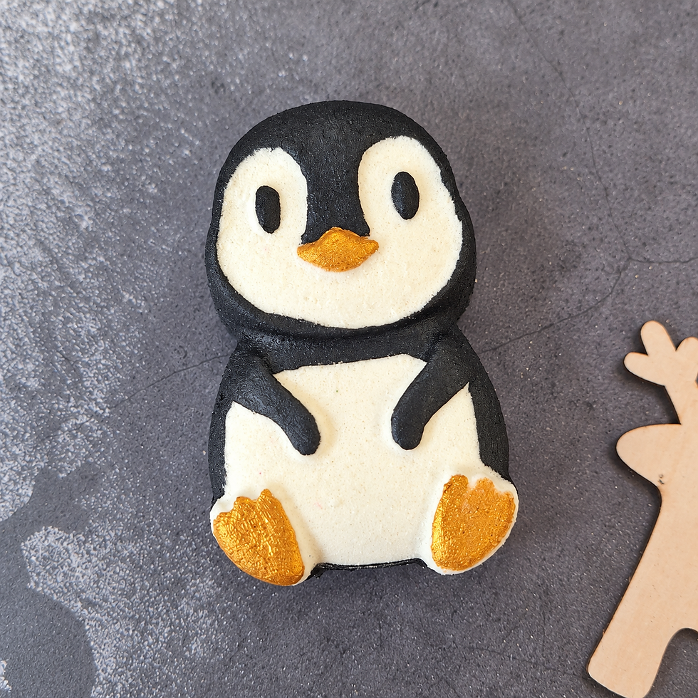 Hand-painted black and white raspberry penguin bath bomb with gold beak and feet on a grey festive background